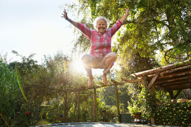 senior woman, 60 yeas old, with overweight, but enjoying to jump on trampoline in garden, file contains lens flares