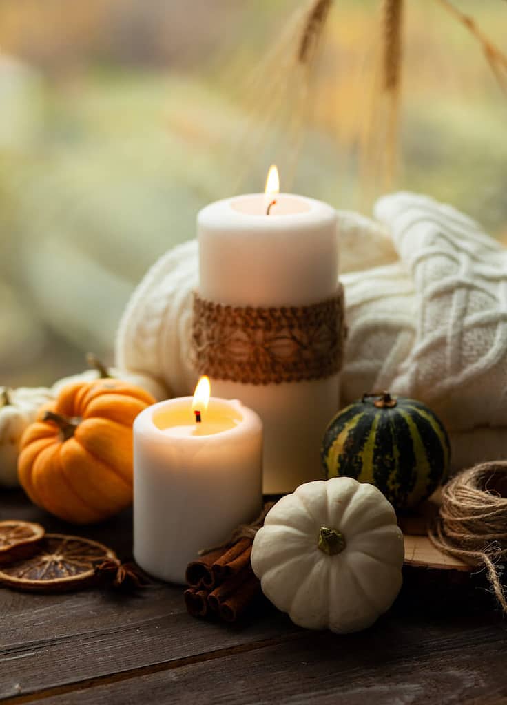 Candles on a wood table next to some pumpkins